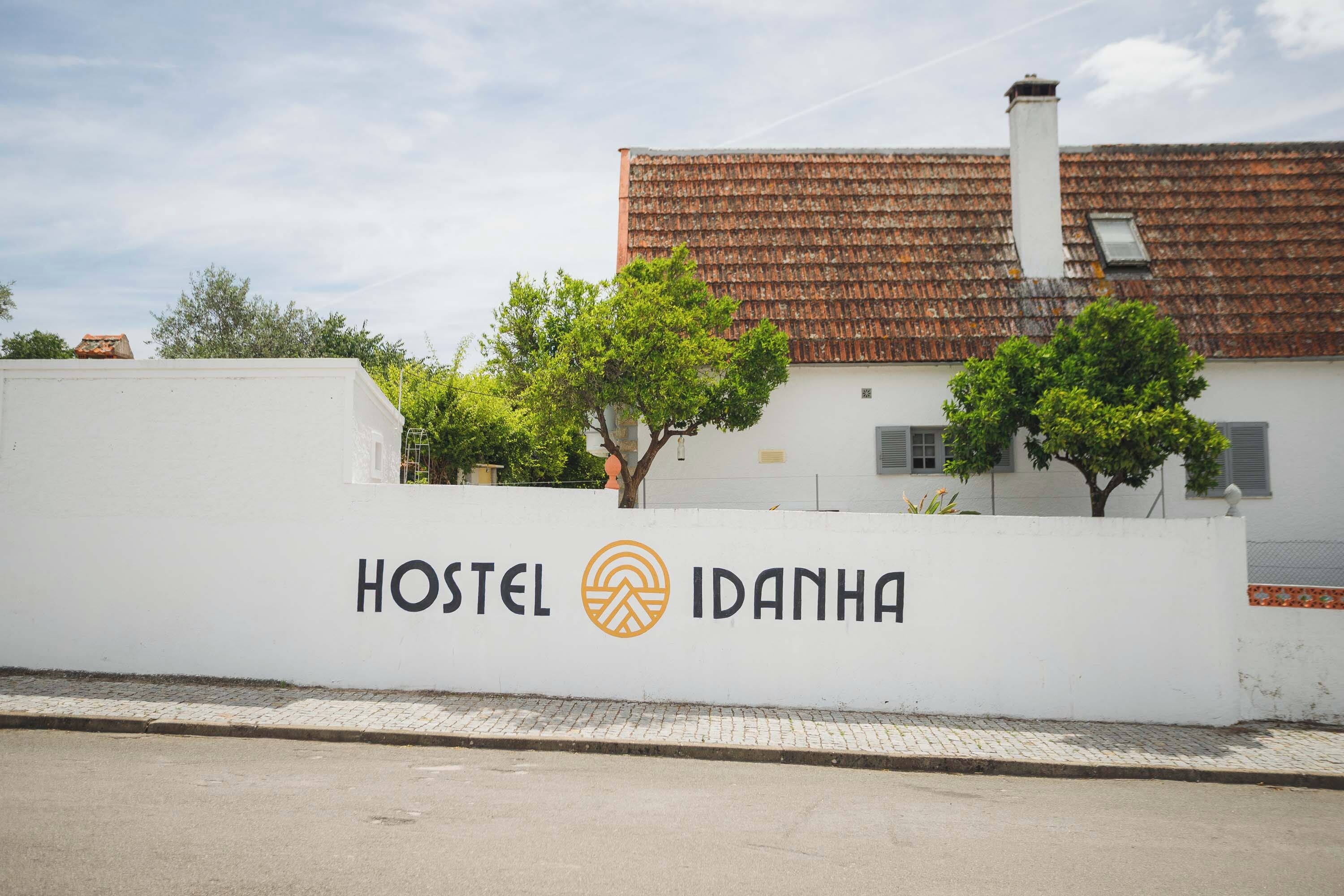 Un hostal llamado 'Hostel Idanha' con una pared exterior blanca, un techo de tejas y dos árboles en la fachada.