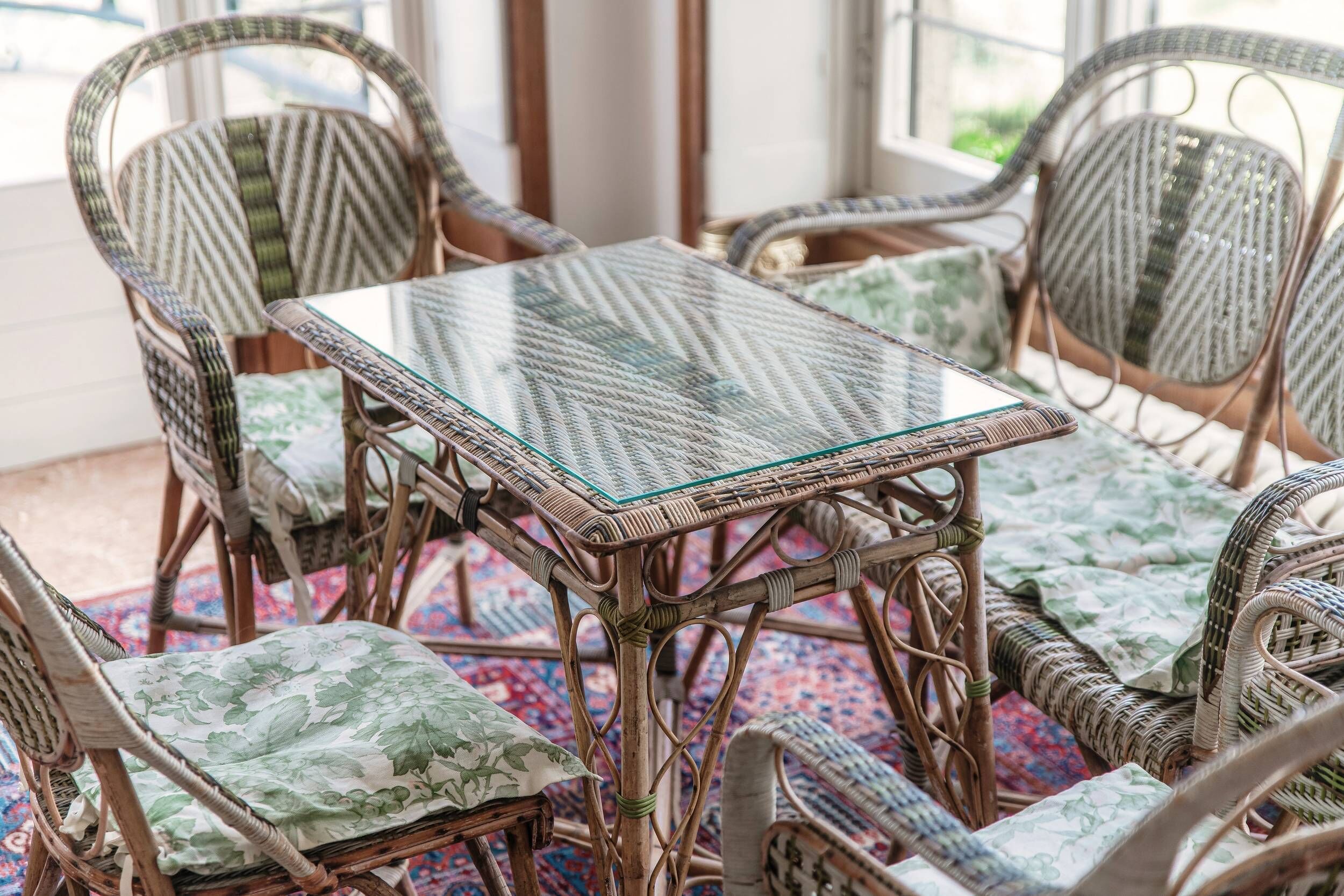 A wicker table with a glass top surrounded by wicker chairs with floral cushions.