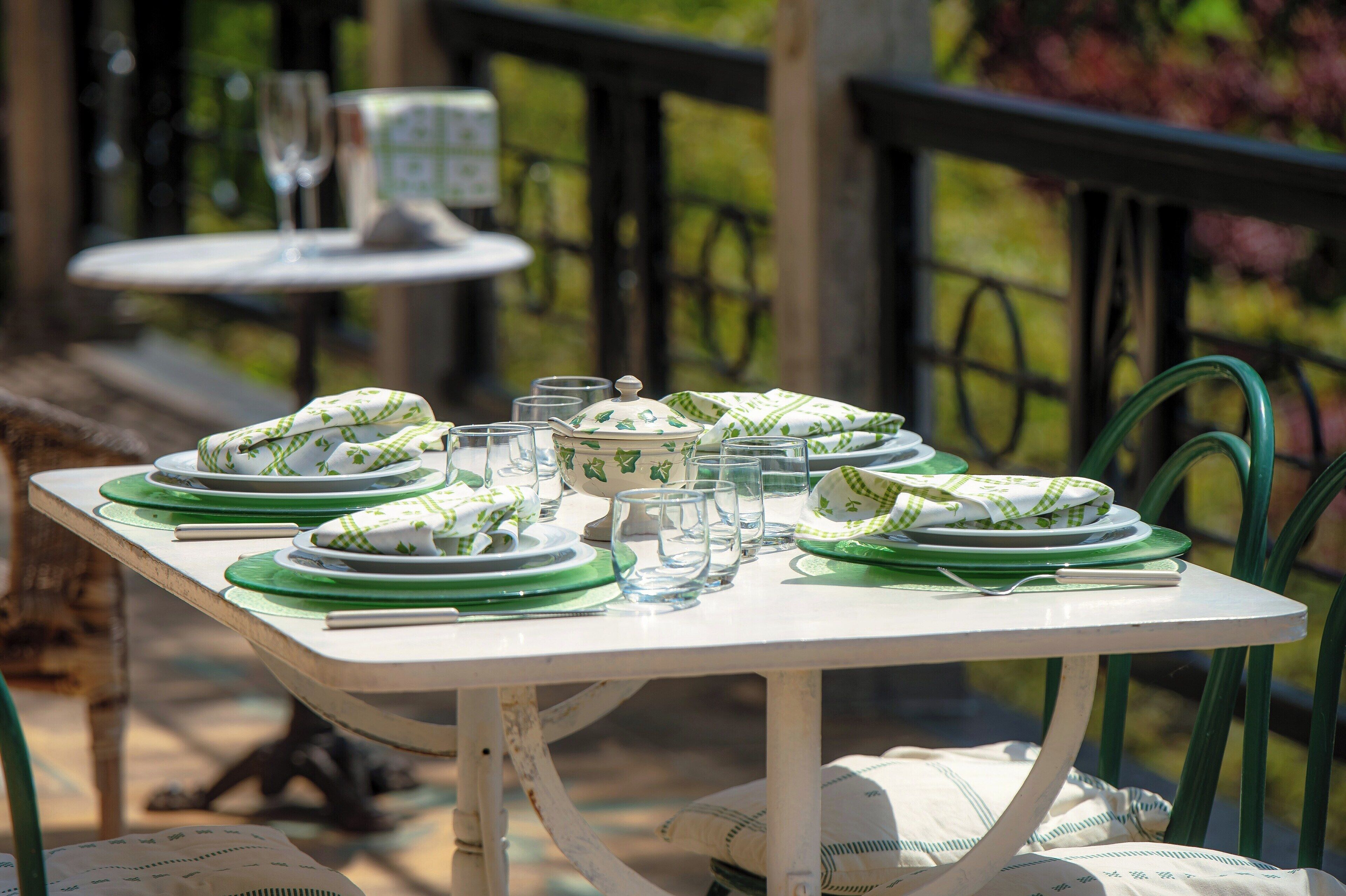 A table set outdoors with green and white plates, bowls, and glasses.