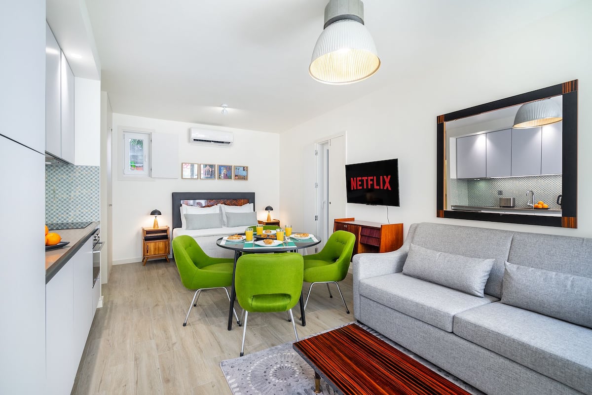 A modern living room with a grey sofa, green chairs, a wooden coffee table, and a TV mounted on the wall.