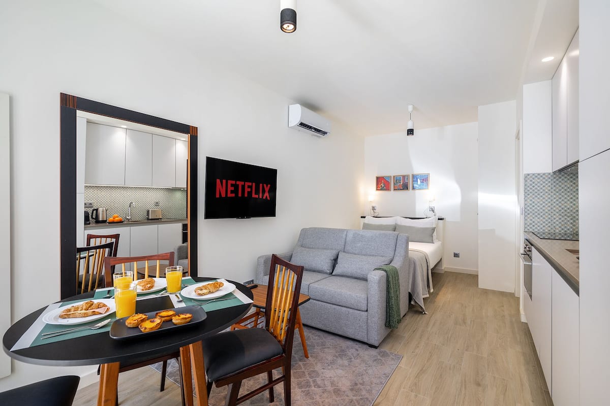 A compact living space with a dining area, kitchenette, and a gray sofa.
