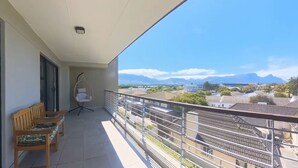A balcony with a wooden bench and a hanging chair, offering a view of houses and mountains. - Immaculate 2-bed Apartment in Cape Town (Cape Town)