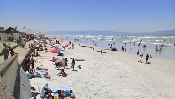 A beach with people sunbathing and swimming, a lifeguard tower, and a clear sky. - Immaculate 2-bed Apartment in Cape Town (Cape Town)