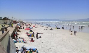 Ein Strand mit badenden Personen, einem Rettungsturm und blauem Himmel.