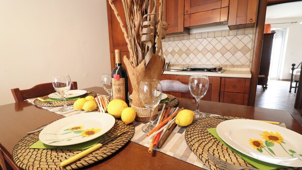 A dining table set with plates, glasses, lemons, and a bottle of wine. - Samiras Home Cozy Apartment Near the Beach and Otrantos Historic Center (Otranto)