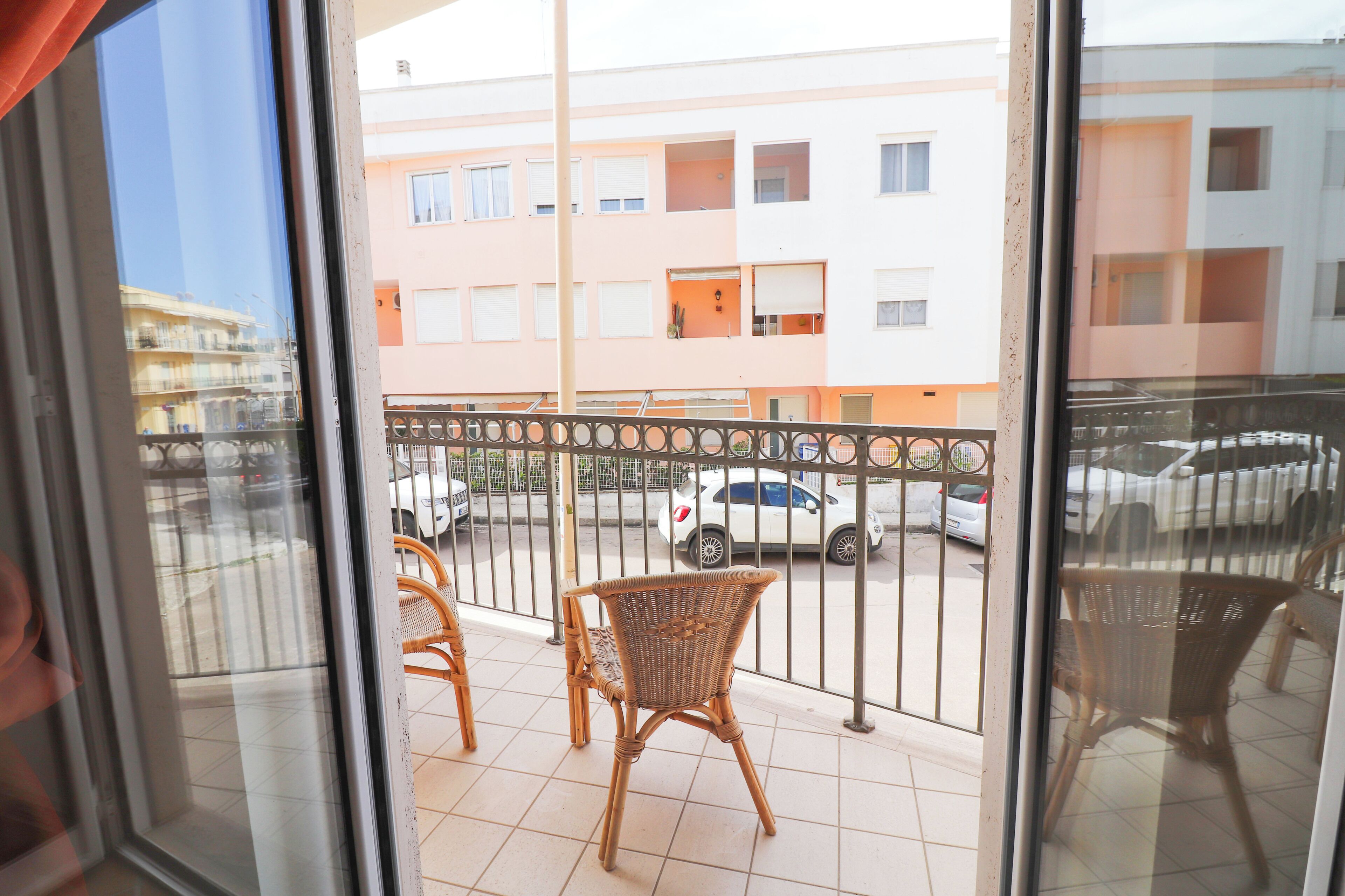 A balcony with wicker chairs, a view of a parking lot, and a building with multiple windows.