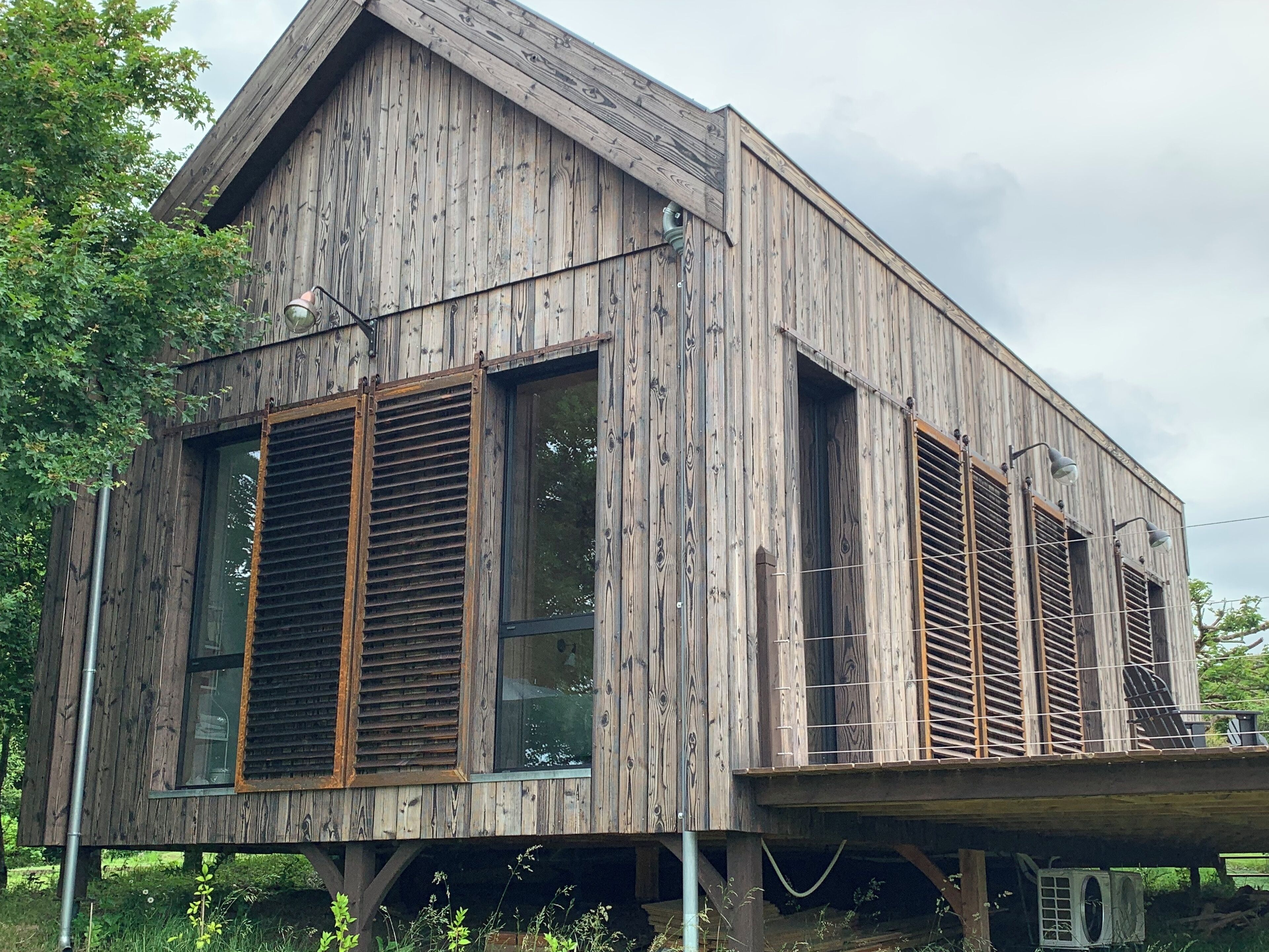 Una casa de madera con ventanas grandes y contraventanas, un techo inclinado y un balcón.