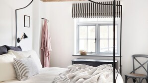 Een slaapkamer met een bed, een raam, een stoel en een nachtkastje.
