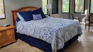 Een slaapkamer met een groot bed, een houten nachtkastje, een plafondventilator en meerdere ramen.