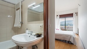 A bathroom with a sink, mirror, and towel rack. The room has a wooden floor and a bed with a view of the outdoors. - Relaxing time near the river (Rio Mau)