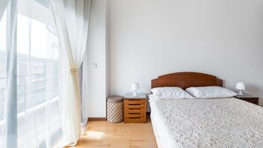 A bedroom with a wooden headboard, a bed with white linens, a bedside table with a lamp, and a small woven basket. - Relaxing time near the river (Rio Mau)