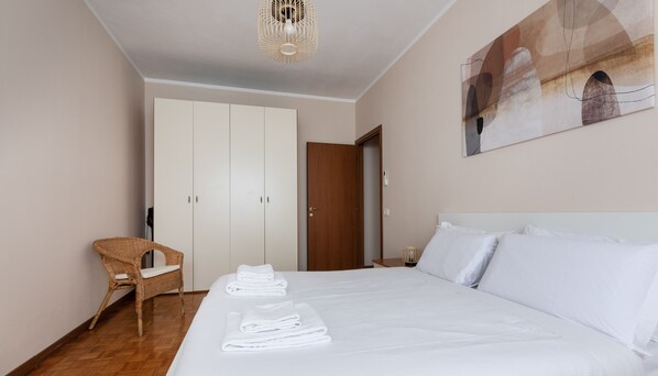 Une chambre d’hôtel avec un grand lit, une chaise en osier, une armoire et un tableau au mur.
