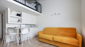 A compact living space with a kitchenette, a sofa, and two white chairs.