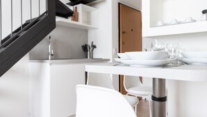 A modern kitchen with white cabinetry, a stainless steel sink, and a dining table set with white plates and glasses.
