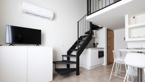 A modern kitchen with a black staircase, white cabinetry, and a flat-screen TV.