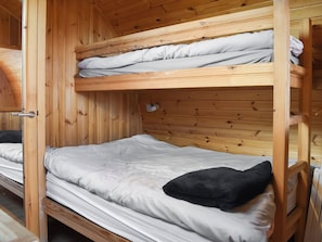 Ein Zimmer mit einem hölzernen Etagenbett, einer Tür, einem kleinen Regal und einem schwarzen Kissen im unteren Bett.