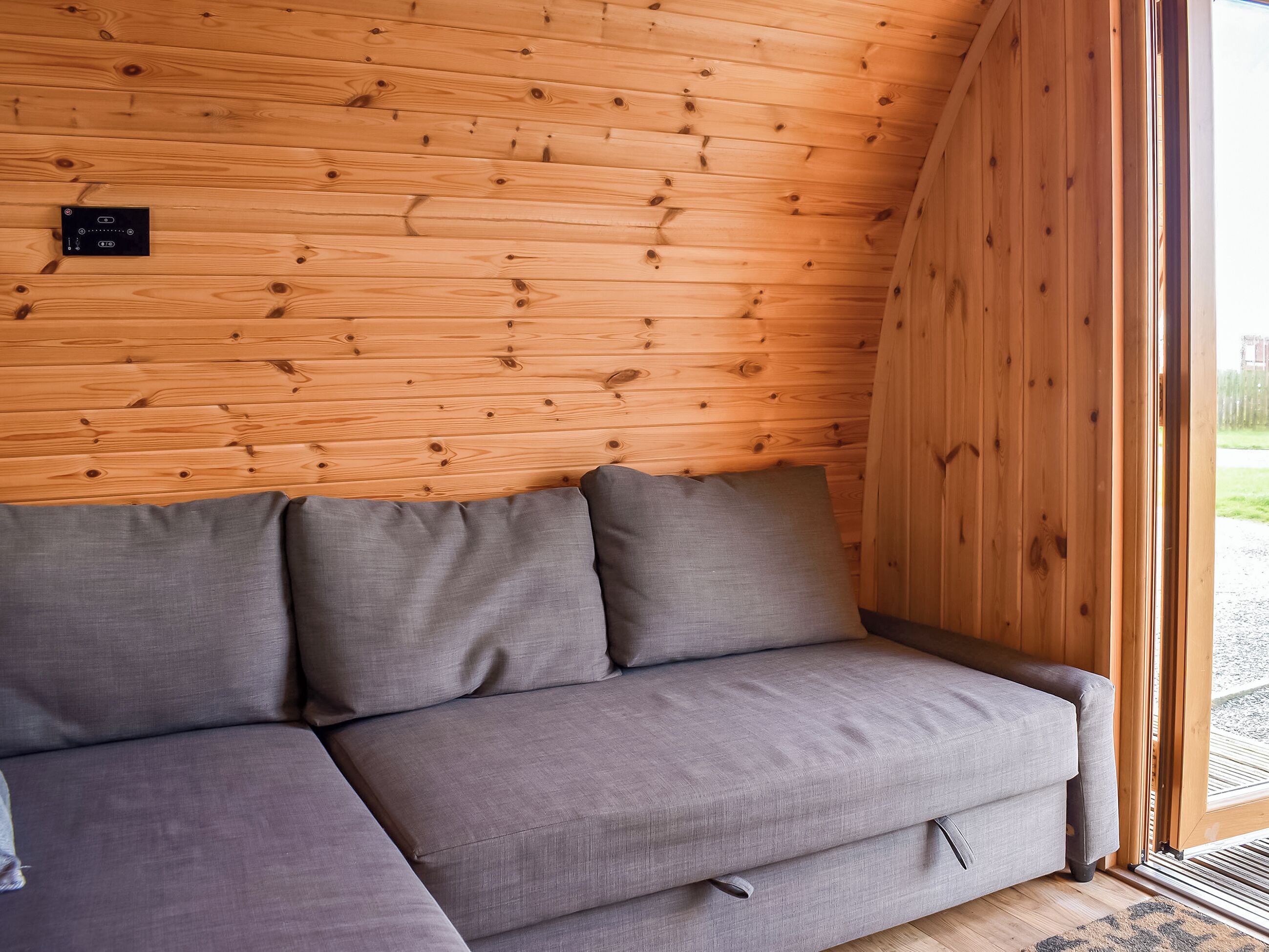 Un interior de madera con un sofá gris frente a una pared de madera.