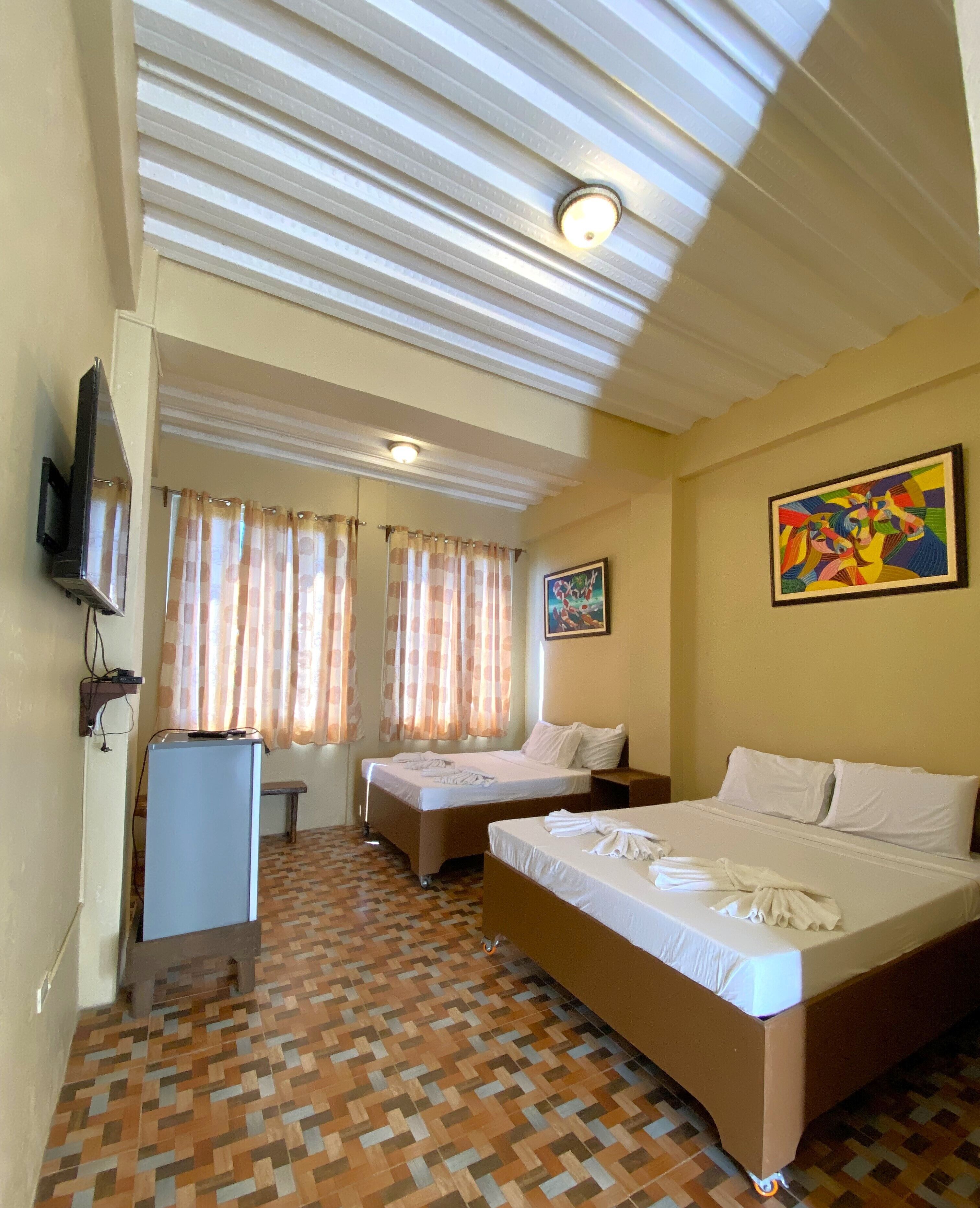 A hotel room with two beds, a television, a desk, and a patterned floor.