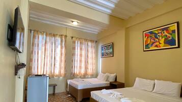 A hotel room with two beds, a television, a desk, and a patterned floor.