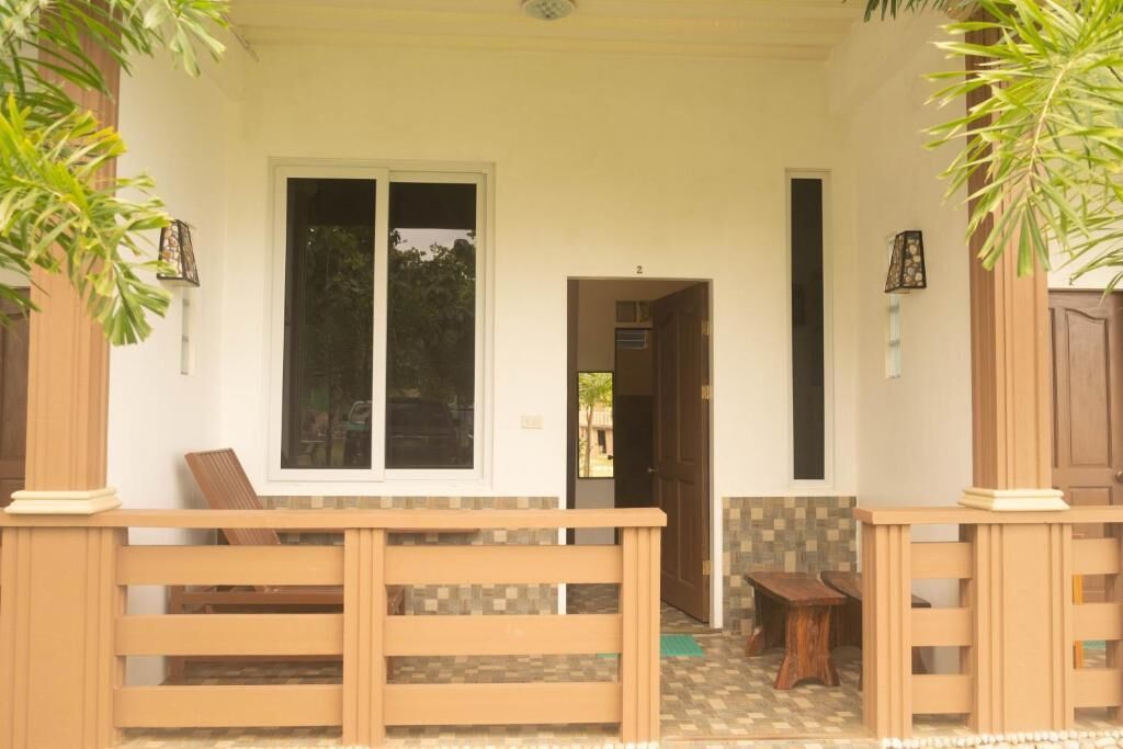 A wooden bench outside a building with a tiled floor and a door leading to an interior space.