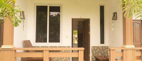 A wooden bench outside a building with a tiled floor and a door leading to an interior space.