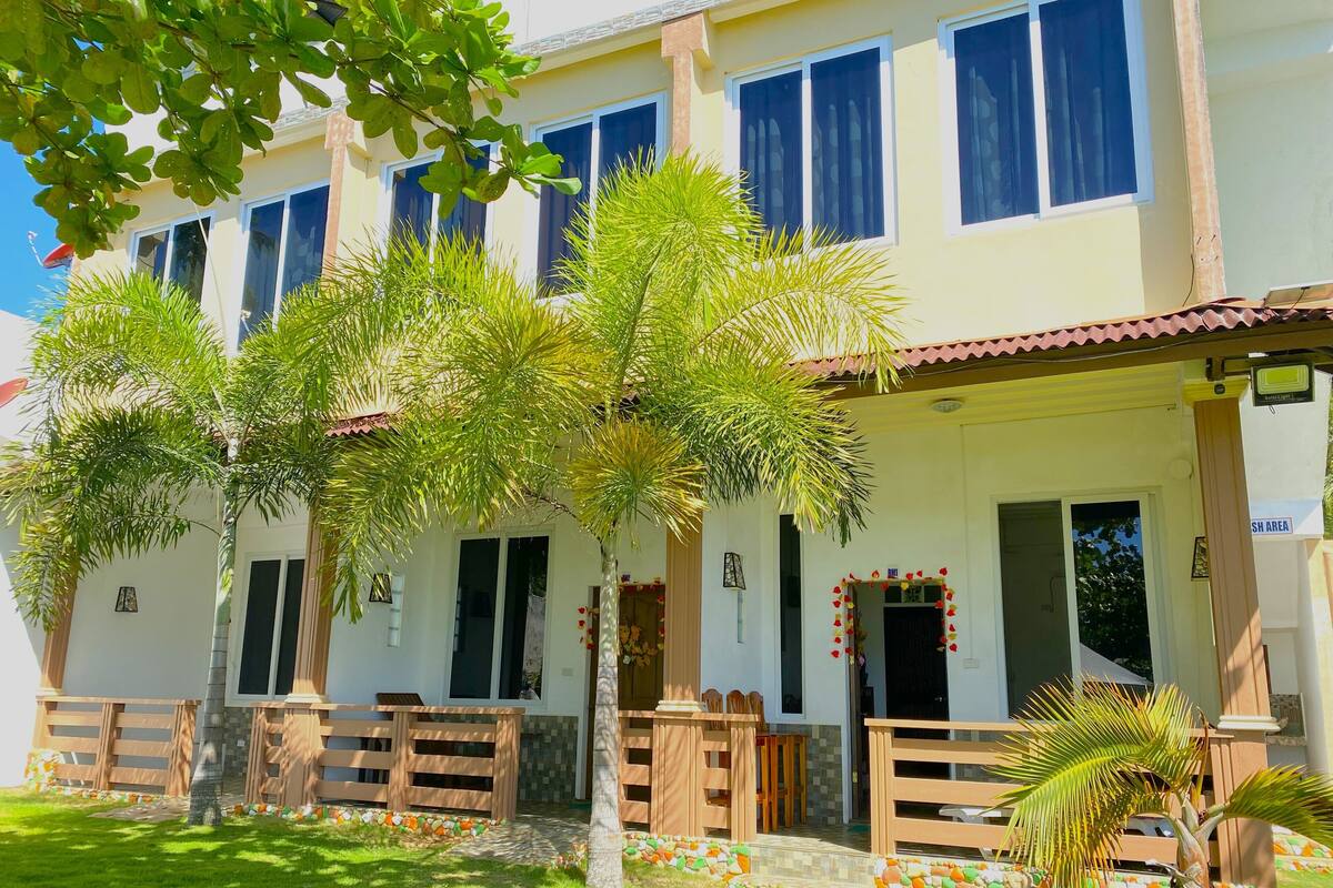 A two-story building with a tiled roof, multiple windows, and a front porch with wooden railings.