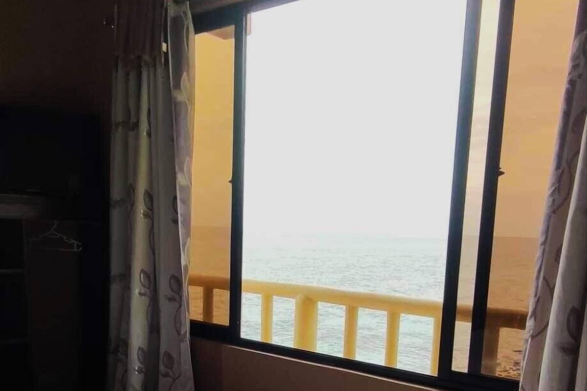 A room with a bed, a window with a view of the sea, and curtains.