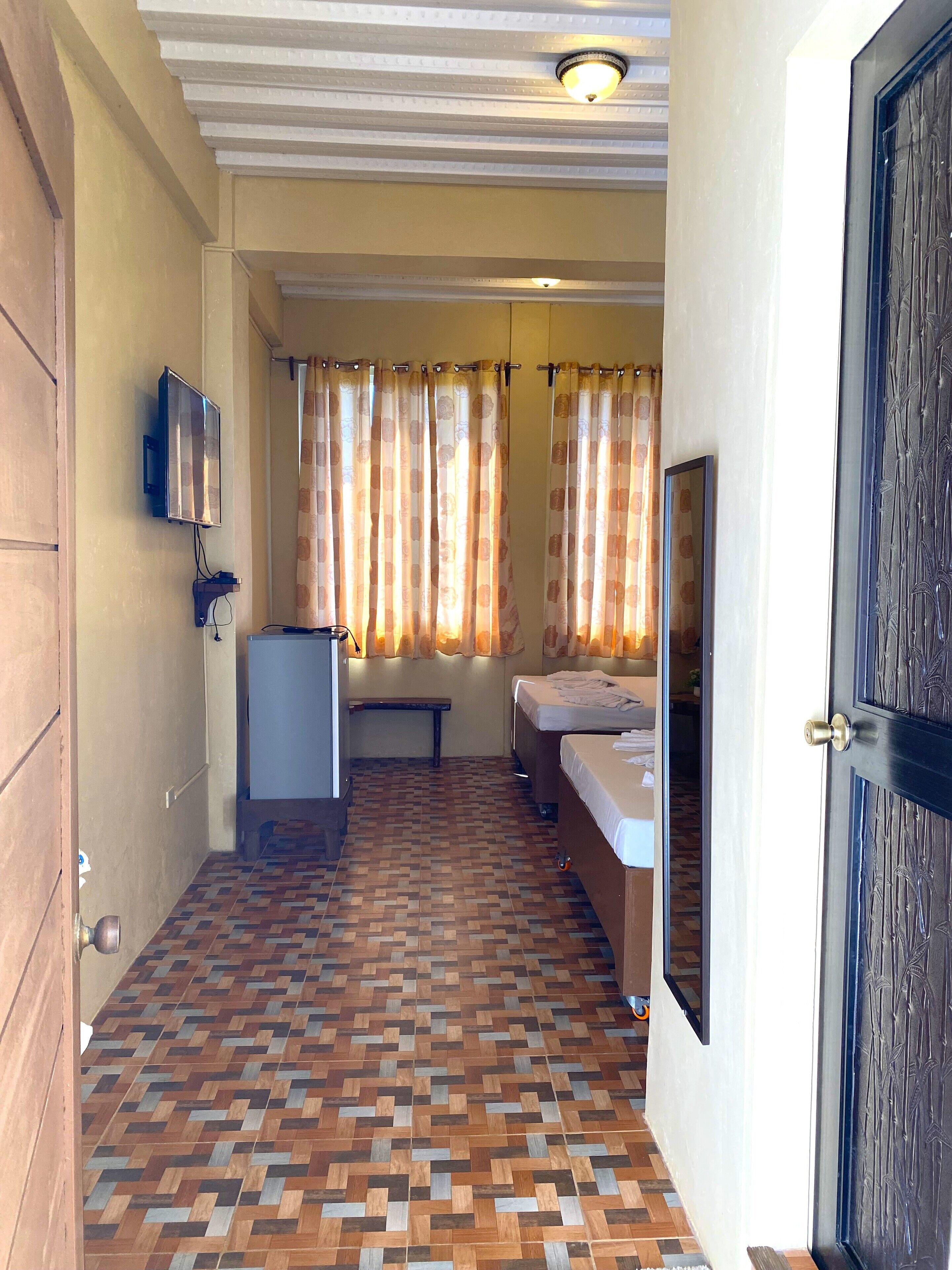 A hotel room with a patterned floor, a bed, a bench, a TV, and curtains.
