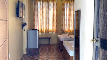 A hotel room with a patterned floor, a bed, a bench, a TV, and curtains.