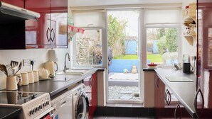 Eine kleine Küche mit Waschmaschine, Spüle und Fenster zum Garten.
