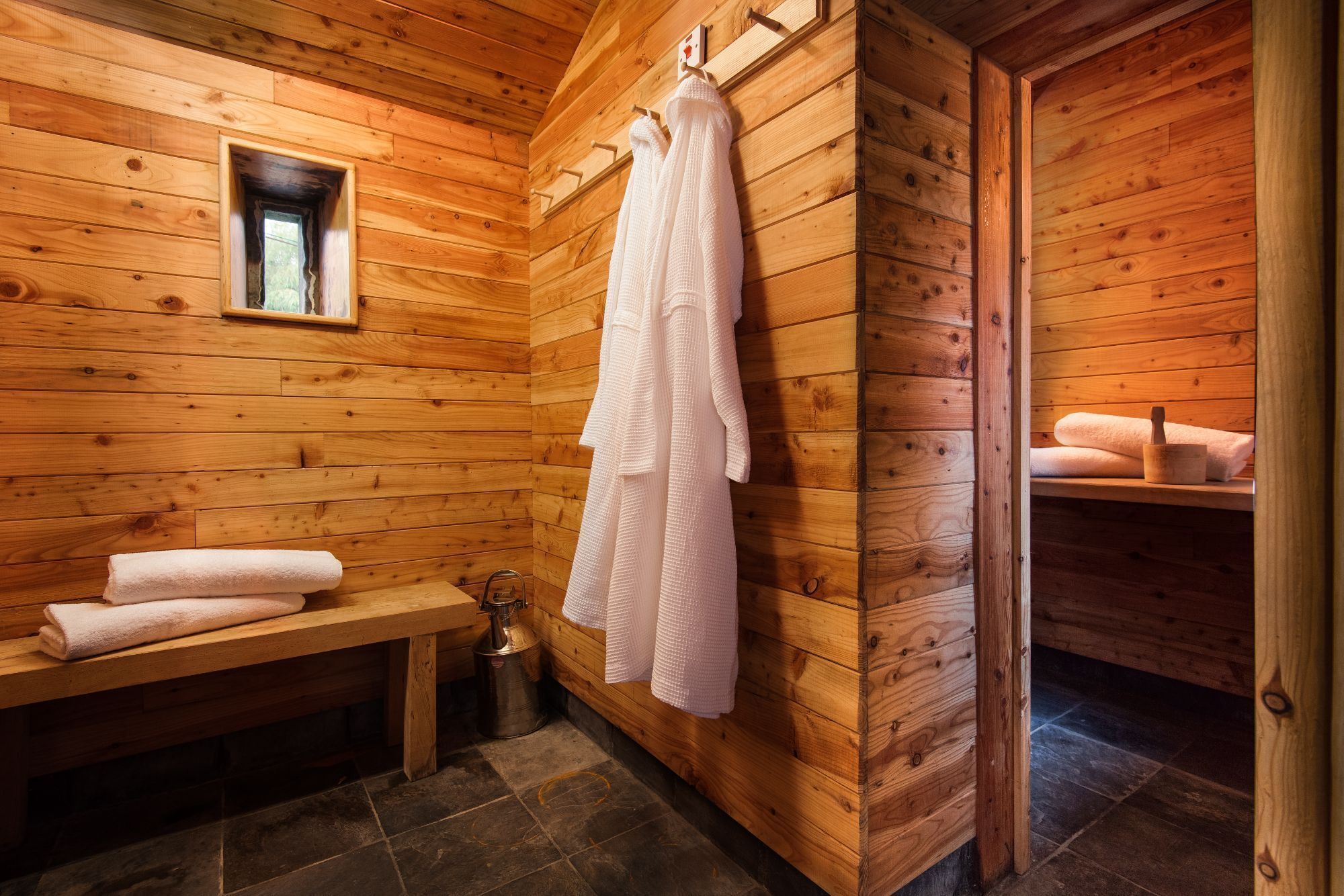 Baño de cabaña de madera con un banco, toallas y una pared de madera.
