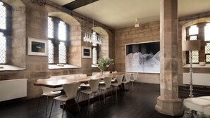 Una amplia sala de conferencias con una larga mesa de madera, sillas blancas y ventanas grandes con arcos.