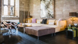 Una sala de estar moderna con sofá, reposapiés y un cuadro abstracto grande en la pared.