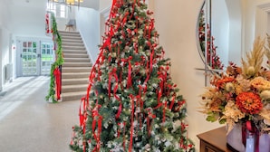 Una imponente escalera que conduce a un segundo piso, un gran árbol de Navidad con cintas rojas y un espejo que refleja el árbol.