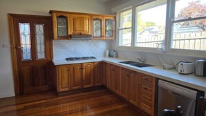A kitchen with wooden cabinets, a gas stove, a sink, and a dishwasher. - Pakenham Villa (Pakenham)