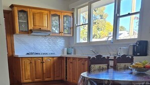 A spacious kitchen with wooden cabinets, a large window, and a dining table with a protective cover. - Pakenham Villa (Pakenham)