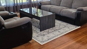 A modern living room with a grey sofa, a black armchair, and a glass coffee table. - Pakenham Villa (Pakenham)