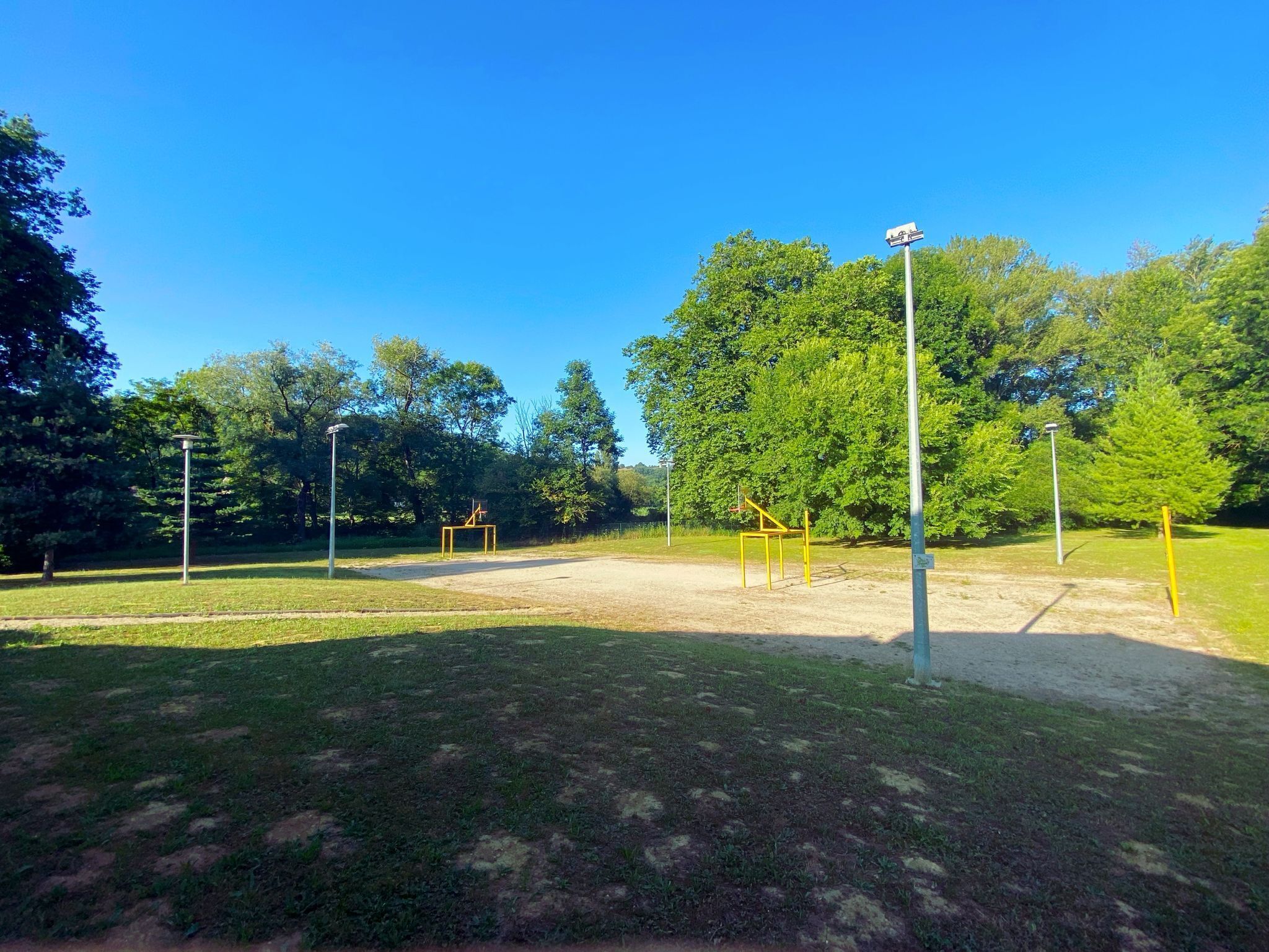 Un espacio al aire libre en un parque con equipamiento para ejercicios, árboles y farolas.