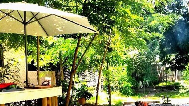 Un espacio de comedor al aire libre con una mesa dispuesta para dos, rodeado de abundante vegetación y un hogar de piedra.