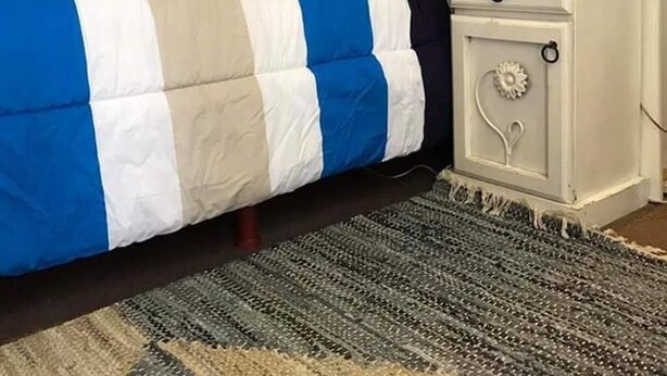 Un lit avec une couvre-lit à rayures, une table de chevet blanche avec une lampe et un tapis à motifs.