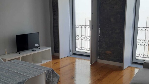 Un salon moderne avec un téléviseur à écran plat posé sur un meuble blanc, une table à manger avec des chaises et un grand canapé gris.