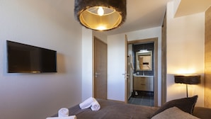 Een hotelkamer met een bed, een flatscreen televisie aan de muur, een deur naar de badkamer en een lampje op het nachtkastje.