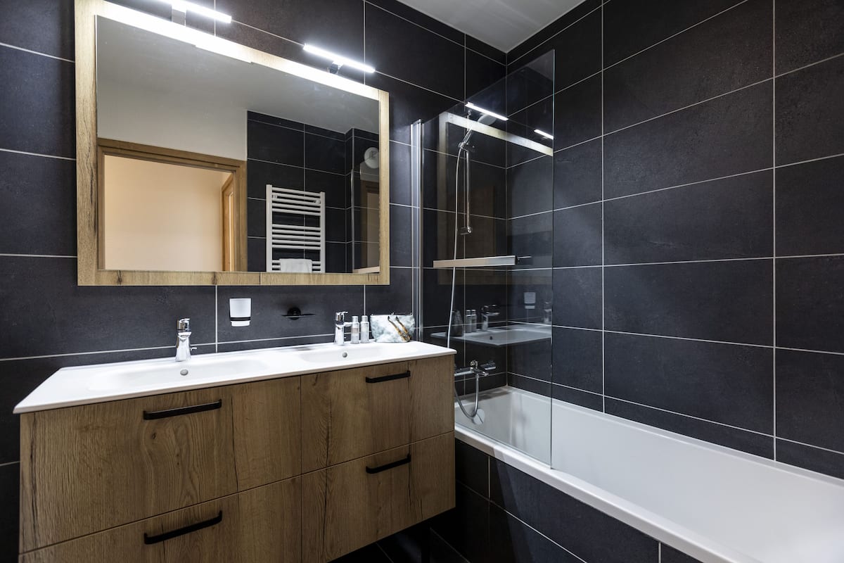 A modern bathroom with a large mirror, a wooden vanity, a bathtub, and a shower area.