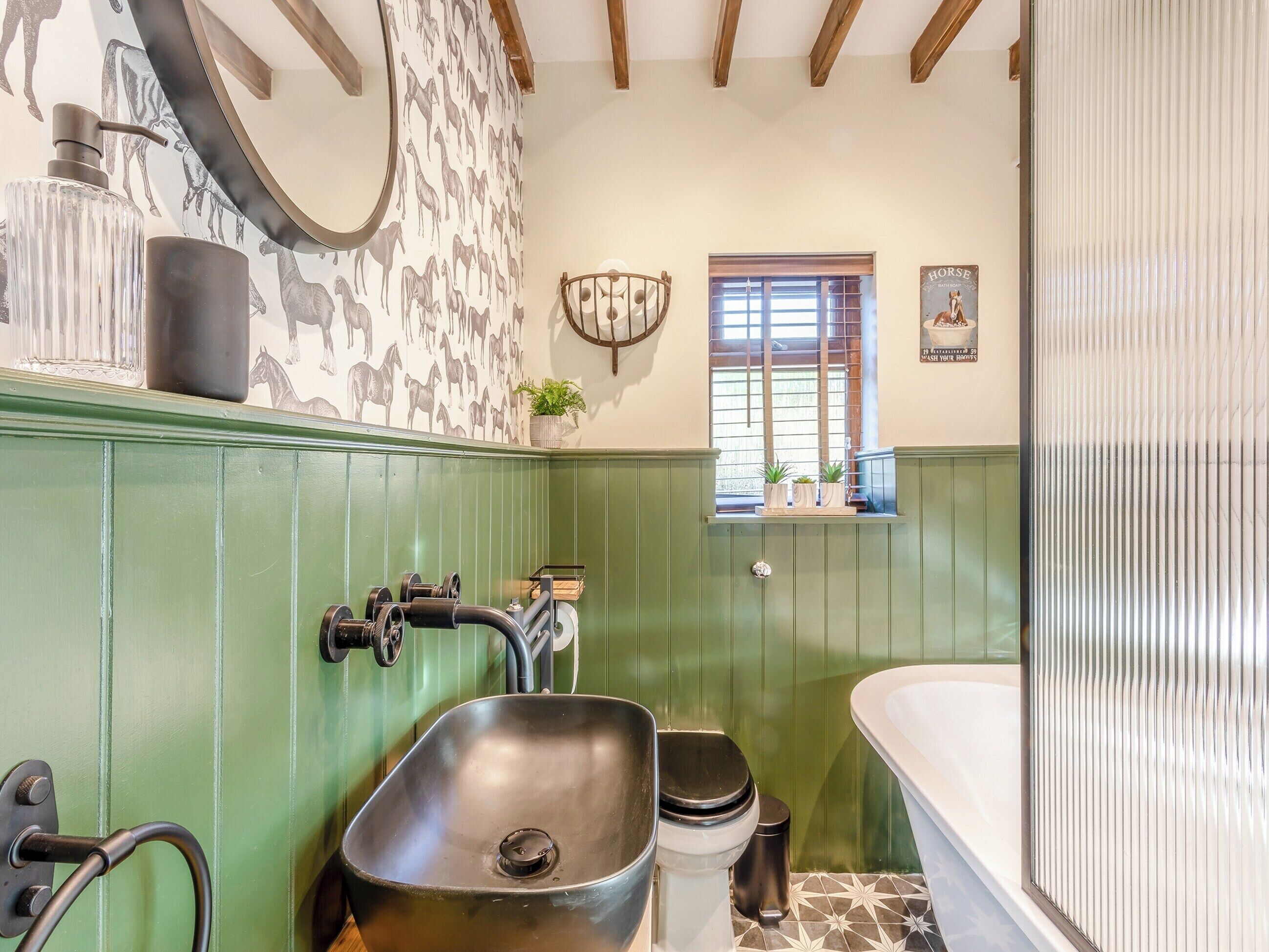 Ein Badezimmer mit einem grünen Waschtisch, einem Waschbecken, einer Toilette und einer Badewanne. Ein Fenster mit Jalousien und ein wandmontierter Spiegel sind vorhanden.