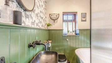 Ein Badezimmer mit einem grünen Waschtisch, einem Waschbecken, einer Toilette und einer Badewanne. Ein Fenster mit Jalousien und ein wandmontierter Spiegel sind vorhanden.