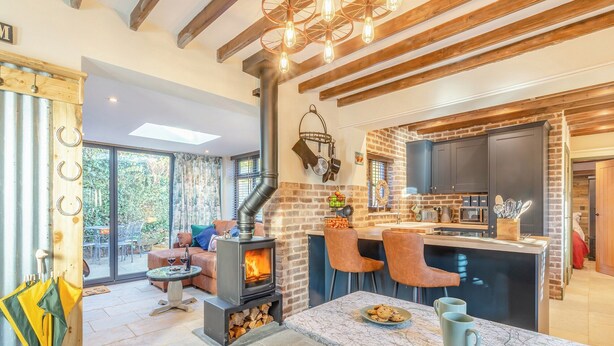Una sala de estar acogedora con chimenea, un comedor y una cocina con pared de ladrillo y vigas de madera.