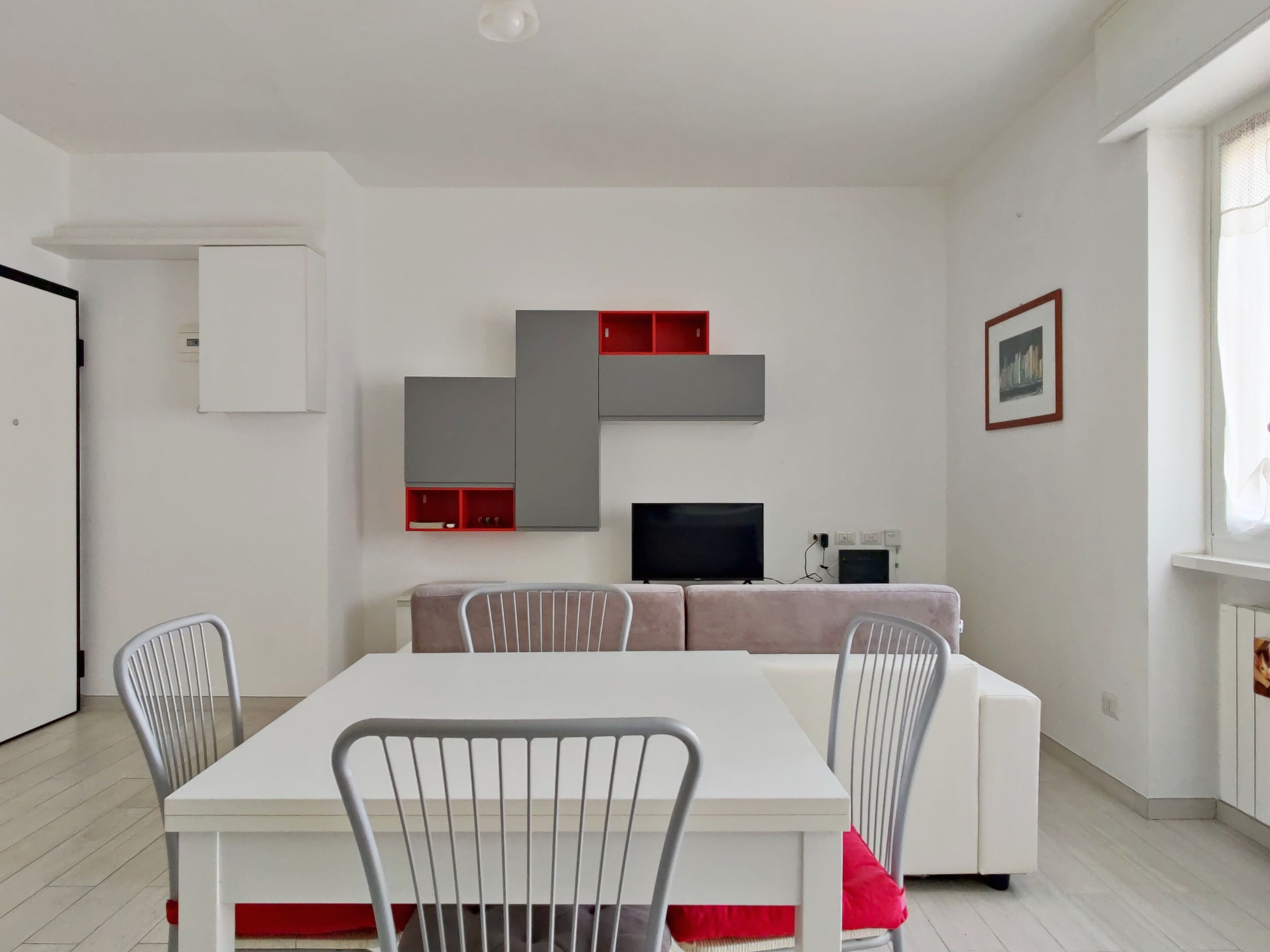A modern living room with a white sofa, a TV, and a dining table with chairs.