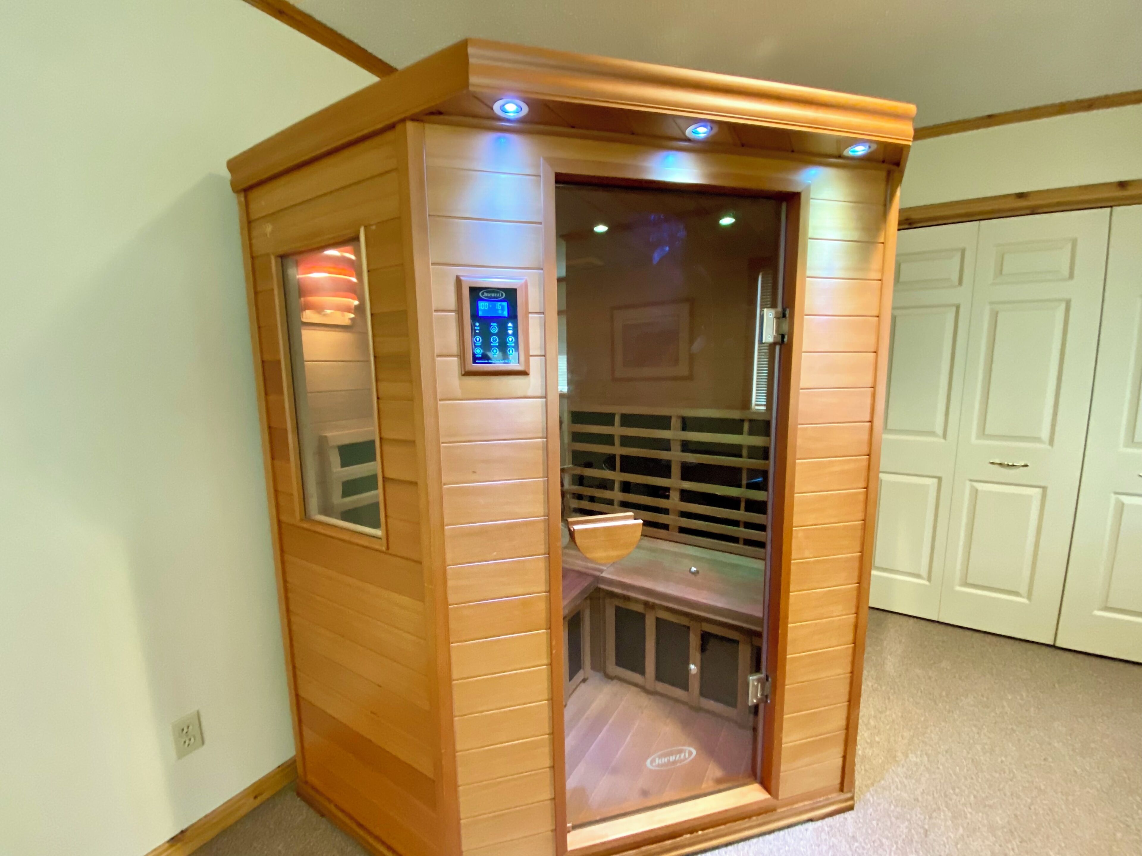 Una sauna in legno con pannello di controllo, porta in vetro e una panca all'interno.