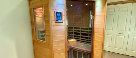 Una sauna in legno con pannello di controllo, porta in vetro e una panca all'interno.