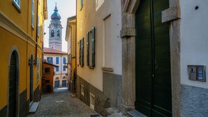 Une ruelle étroite pavée de pierres, bordée de bâtiments des deux côtés, avec une porte verte et, au loin, un clocher.